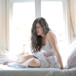 Mujer sentada en la cama de casa con una mano en el abdomen por una molestia leve
